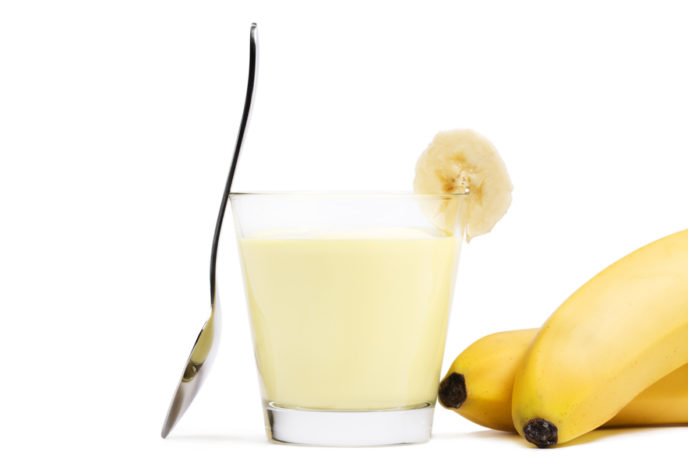 Banana milkshake with a piece of banana a spoon and bananas aside