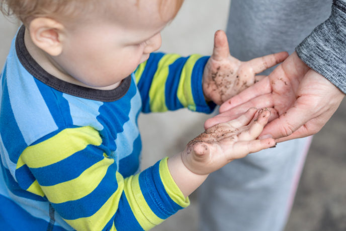 Cute little toddler boy showing mother dirty hands after playing in mud outdoors. Curious child with dirt or soil on palms after discovering world. Hygiene and children healthcare. Washing hands