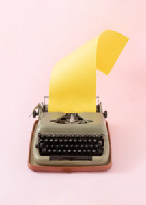 Vintage typewriter with yellow writing paper on pastel pink background. Minimal retro tech concept. Creative copy space.
