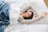 Zobúdzajúca sa žena v posteli prikrytá perinou a dekou.